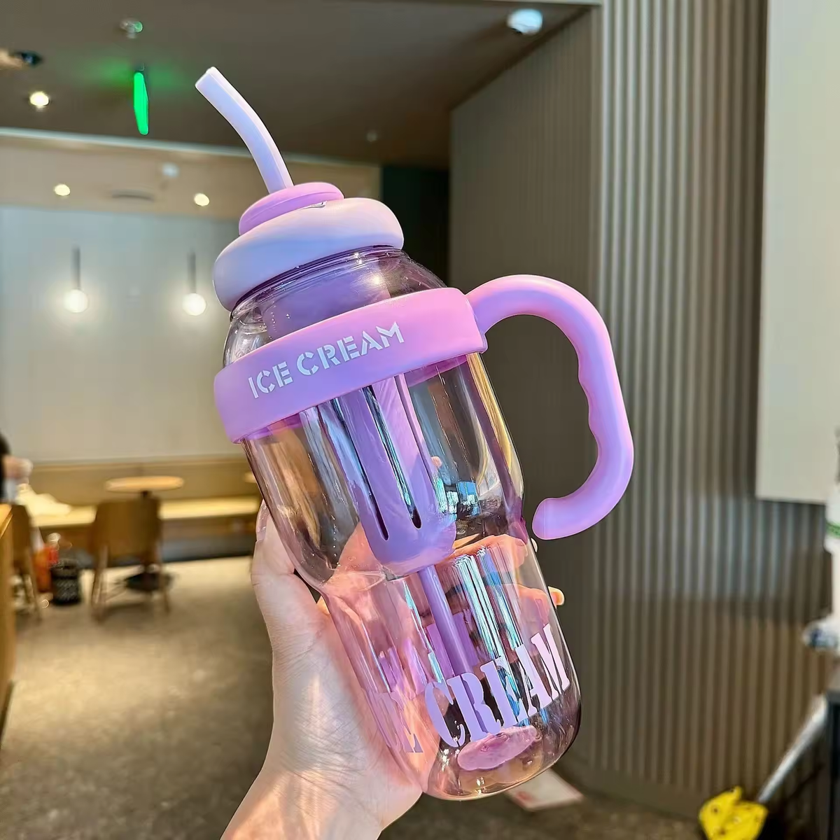 Pink and clear tumbler with handle and straw held in a hand, 
