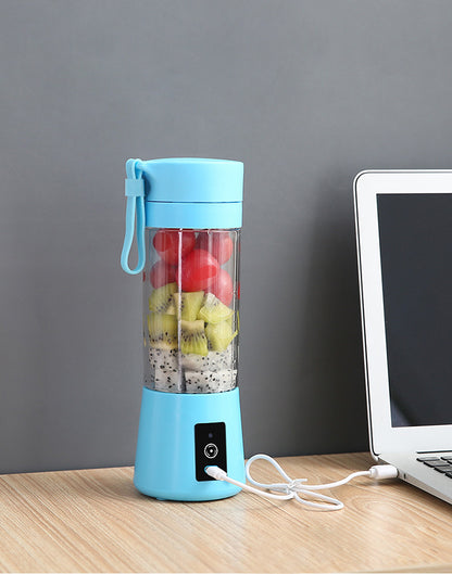 Blue portable blender with fruits inside on a wooden table next to a laptop.